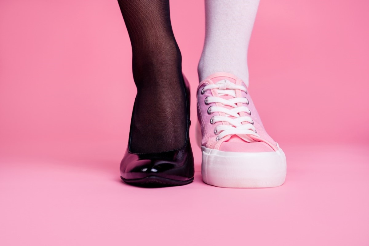 Benen en schoenen, twee benen, één in zwarte zijden kousen met zwarte pumps en de ander in roze kousen en gympen.