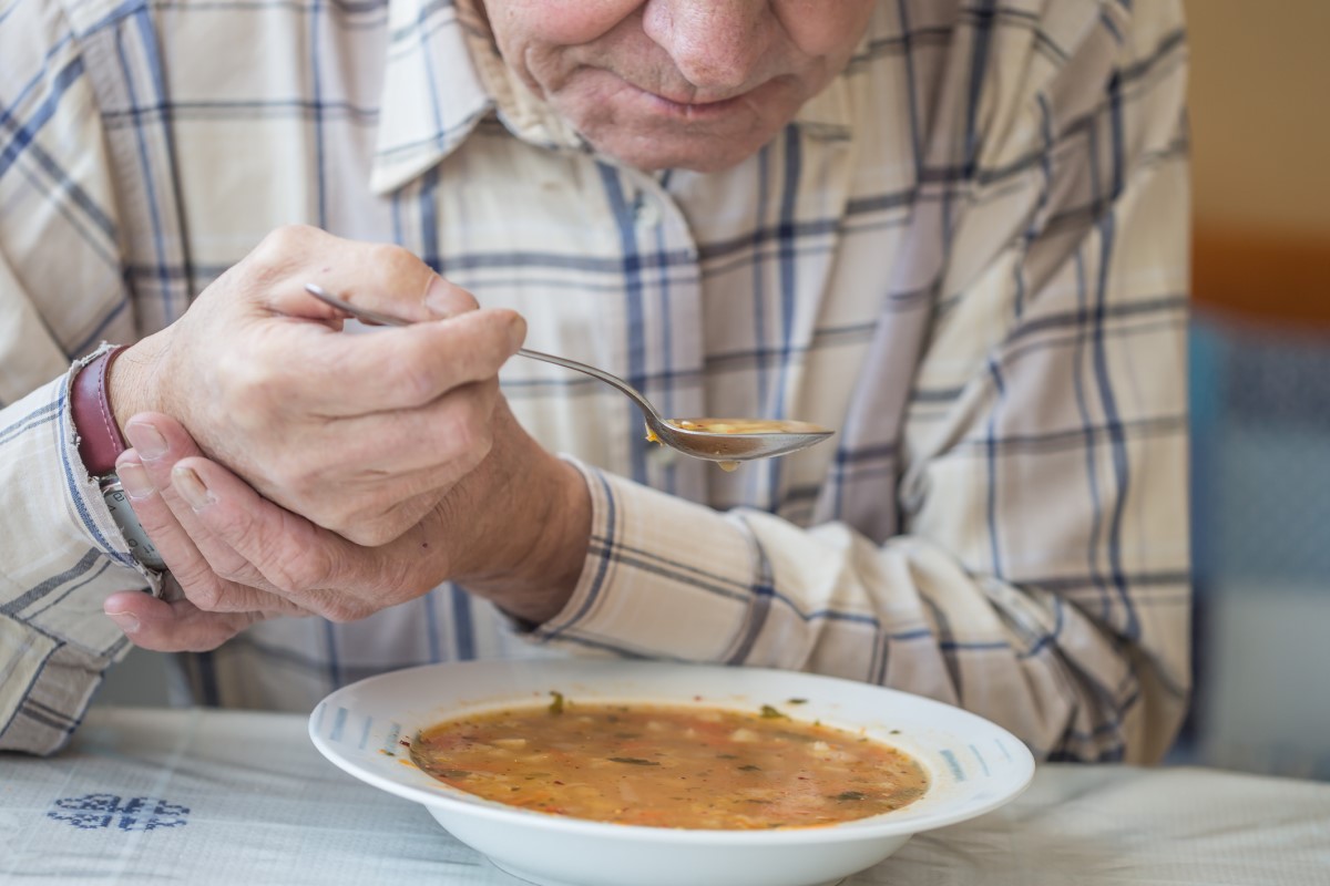 Man eet soep en houdt zijn hand vast tegen tremoren bij Parkinson