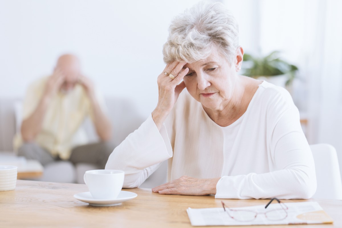 Bejaarde vrouw houdt haar hoofd vast, door achteruitgang van neurologische functies van de hersenen, mogelijk de ziekte van Alzheimer. Bejaarde vrouw op de voorgrond, hoofd gebogen, leunend op haar hand