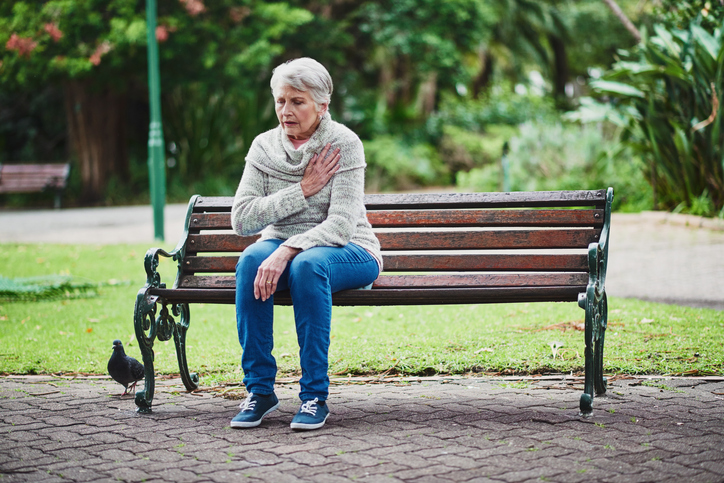 Een oudere vrouw zit op een bankje en heeft hartproblemen.