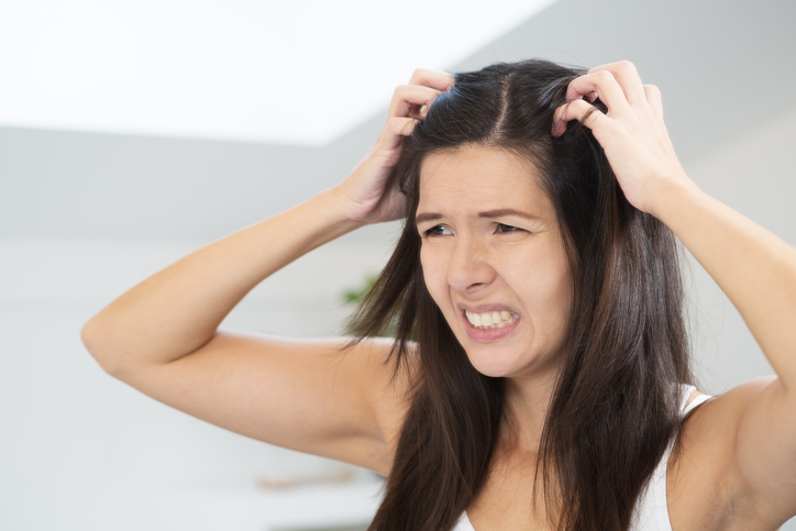 Een vrouw heeft een haarprobleem, roos, een jeukende hoofdhuid, ze krabt aan haar hoofd met haar handen