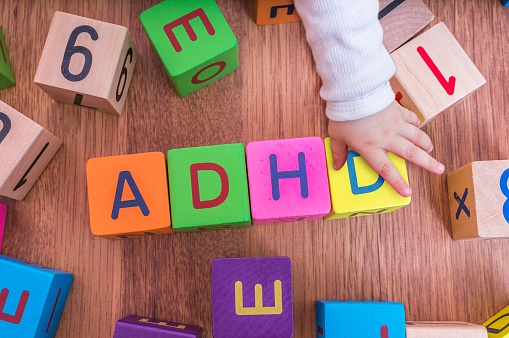 letterblokjes van kinderen, gerangschikt om de naam ADHD te vormen, met de hand van het kind