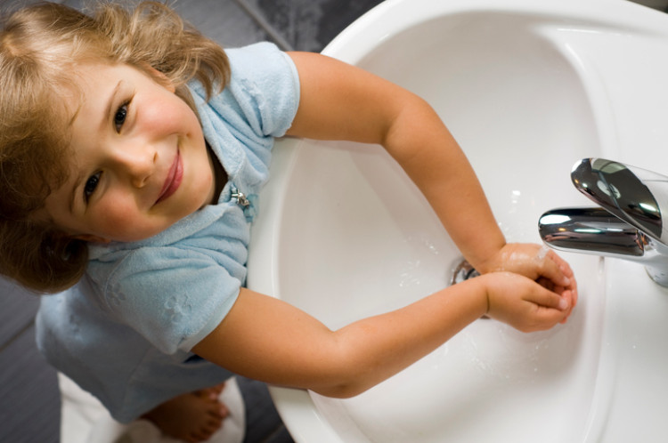 klein meisje wast haar handen met schoon water uit de gootsteen