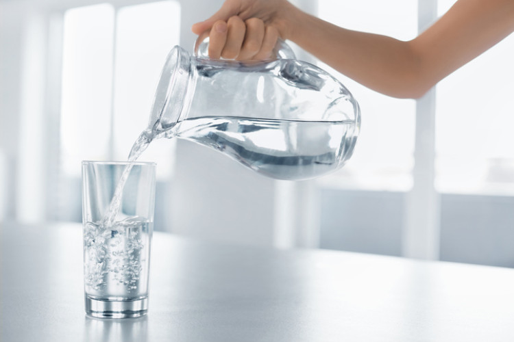 een hand die schoon water uit een fles in een glas giet