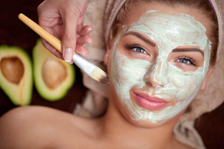 vrouw met een tulband op haar hoofd en een groen natuurlijk masker op haar gezicht, op de achtergrond een gesneden avocado