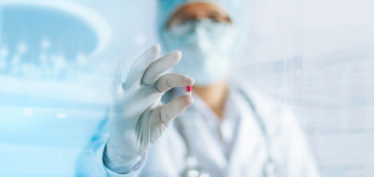 een dokter in een wit uniform met een sluier over haar gezicht die een pil in haar hand houdt