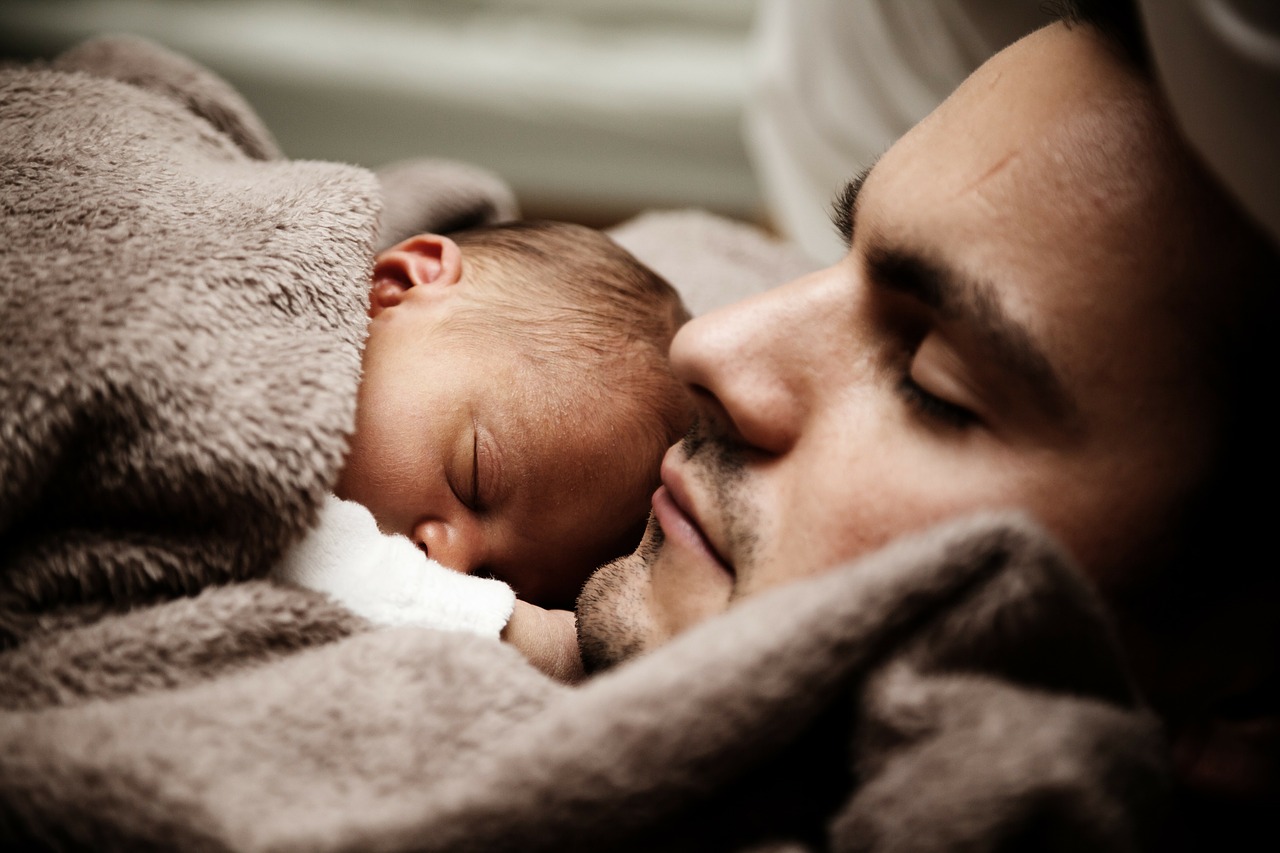 de baby slaapt naast zijn vader onder een bruine deken