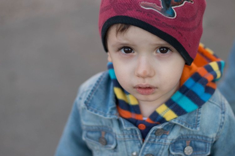 een kind in een blauwe jas en een rode pet kijkt in de lens