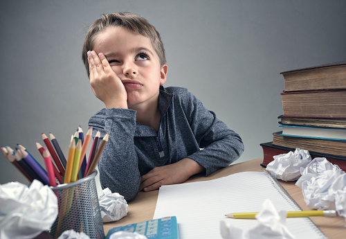 een schooljongen zit aan zijn bureau, denkt na over iets, met een schrift, papier, potloden op zijn bureau