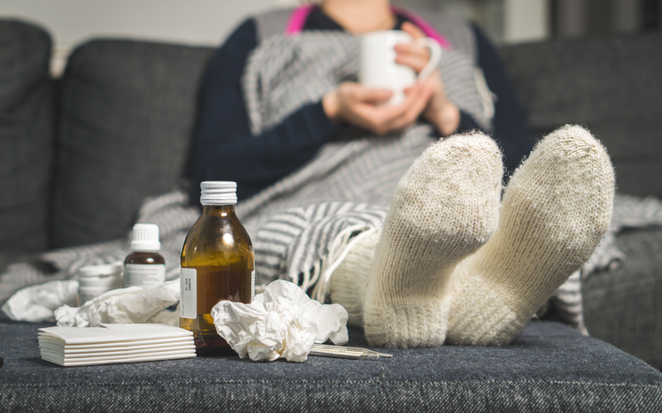 een zieke vrouw ligt in bed met warme sokken en pillen en siropen naast haar