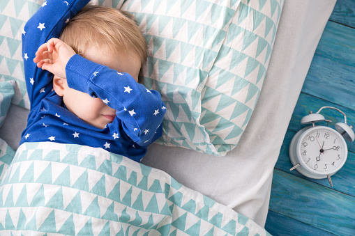 Wakker worden van jongetje in blauwe pyjama, naast de wekker