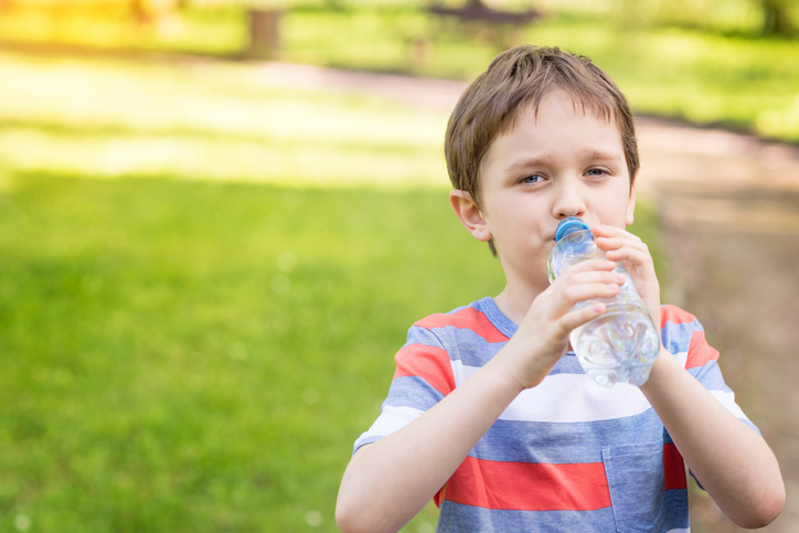 Jongen drinkt water uit fles, groen gras op achtergrond