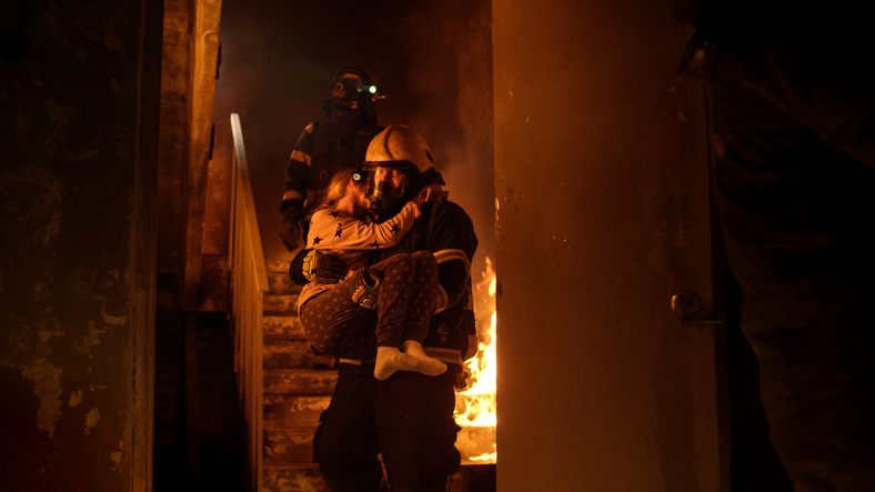 brand in het huis, brandweerlieden dragen het kind in hun armen naar buiten