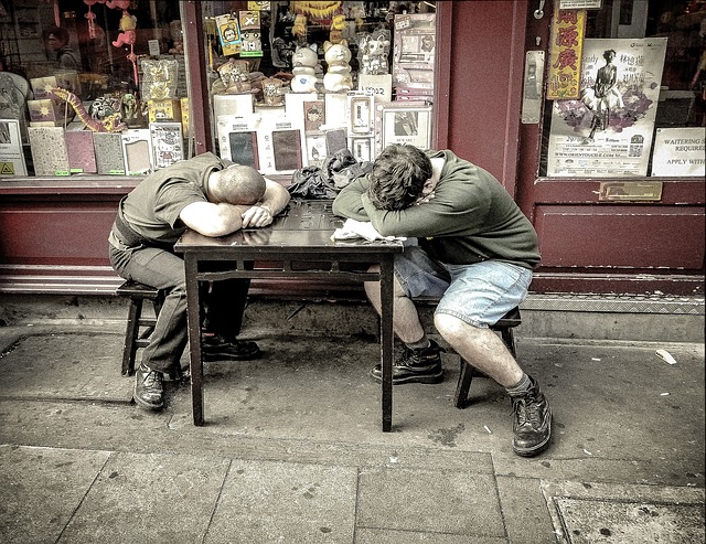 Twee mannen slapen aan een tafel buiten de winkel. Het is een oude winkel.