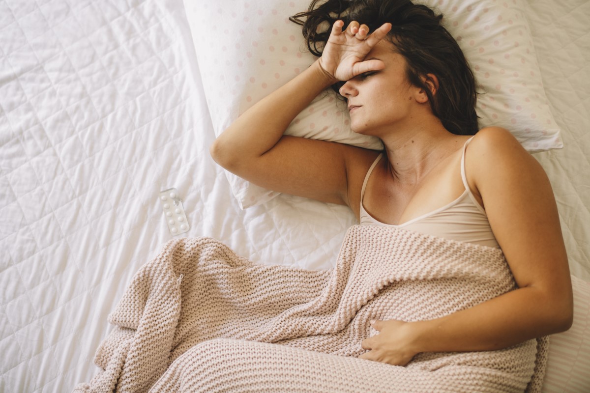 De vrouw lijdt aan migraine, ligt in bed en heeft gezondheidsproblemen.