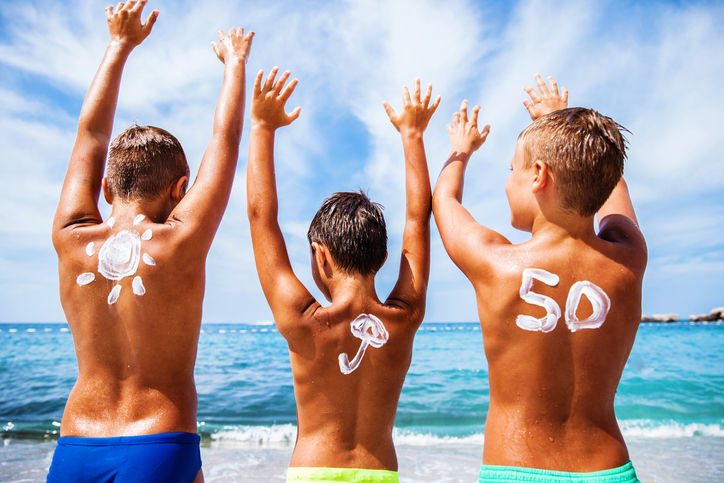 Zonnebrandcrème voor kinderen met OF 50, kinderen zijn op het strand aan zee en genieten, hun handen zijn omhoog