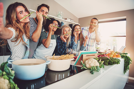 Mensen glimlachen terwijl ze eten bereiden. Ze staan achter het fornuis.