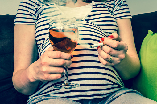 Zwangere vrouw in een gestreept T-shirt met een sigaret en een glas wijn