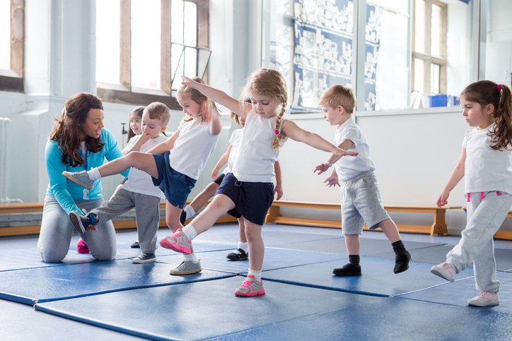 Jonge kinderen in de gymzaal, oefenen met de leraar.