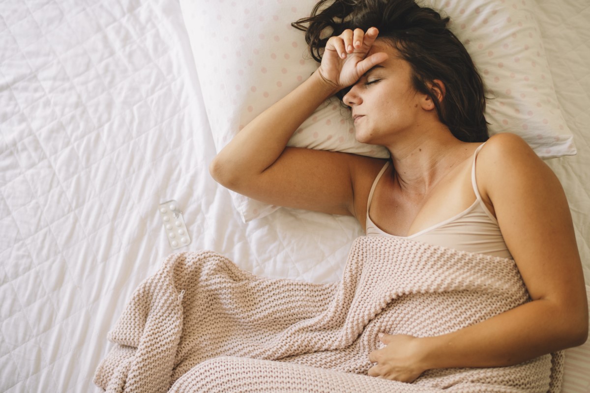 Een vermoeide vrouw ligt in bed, haar maag doet pijn