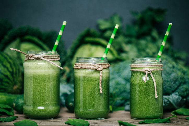 Groene groente smoothie, drie glazen, kool, broccoli en erwten op de achtergrond