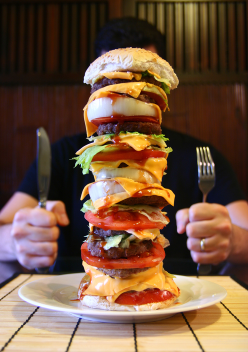 Een man zit aan een tafel met een grote hamburger op zijn bord, een megapower