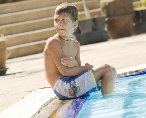 De jongen zit bij het zwembad, zijn voeten in het water. Hij heeft het koud.