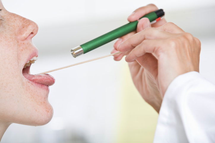 de dokter onderzoekt de keel van de vrouw met een mondhamer en zijn ogen en schijnt met een zaklamp in haar keel