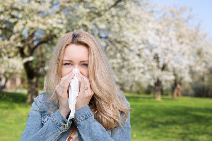 vrouw heeft hooikoorts, niest, is buiten, gras en boombloemen