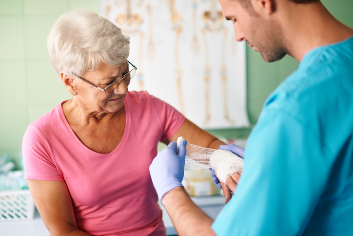 Een vrouw, een senior, heeft een gewonde arm en wordt behandeld door een paramedicus