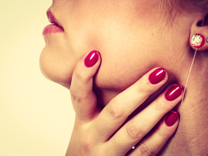 De vrouw houdt haar keel vast, het doet pijn, haar nagels zijn rood gelakt